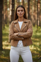 Front view of a tan suede-effect biker jacket worn over a white top and white jeans, arms crossed showing zip cuffs.