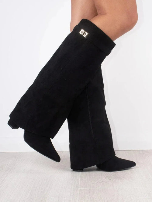 Side view of black suede knee-high fold-over boots with pointed toe and gold buckle detail at the cuff