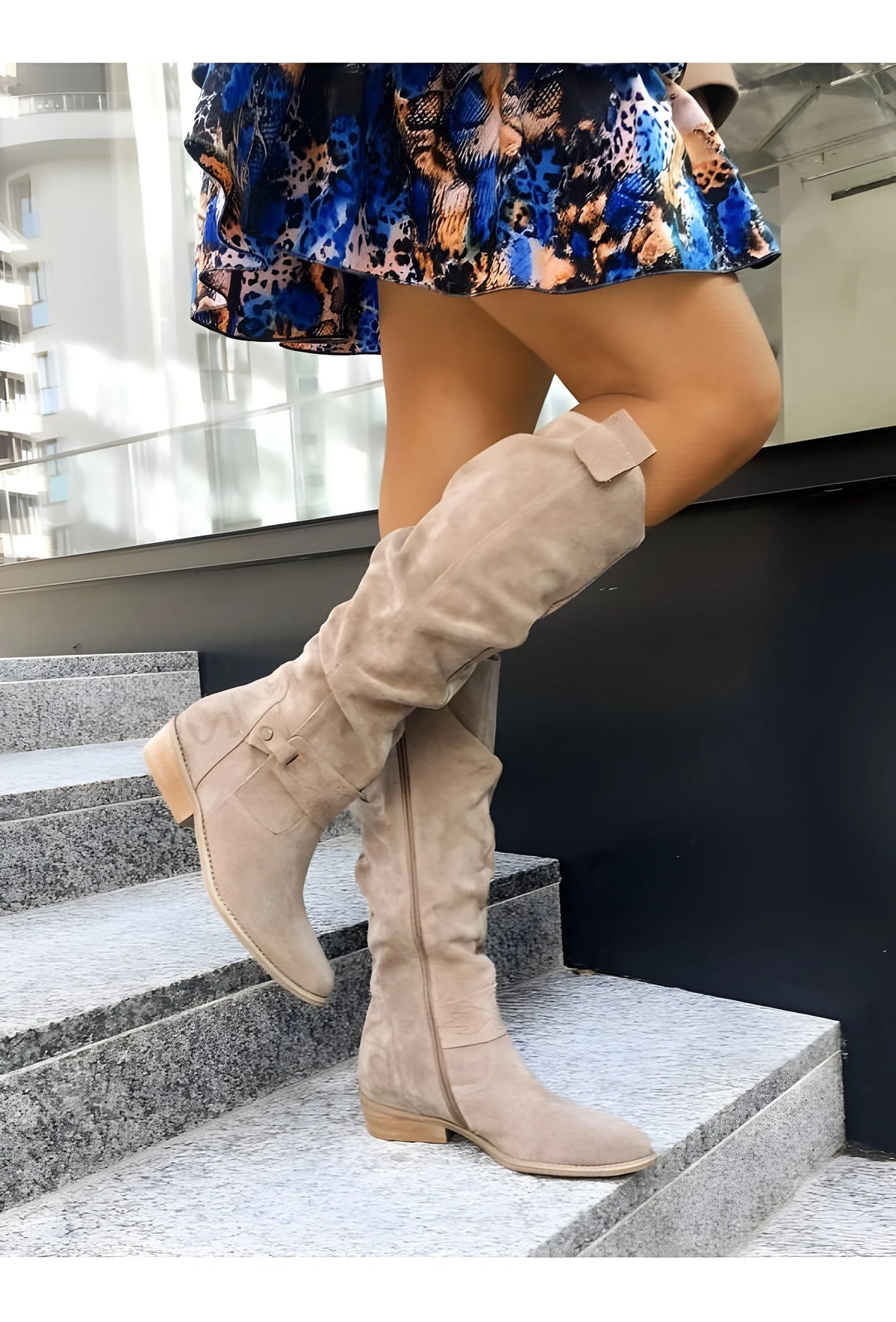 Beige suede knee-high boots with pull tab and side zip, worn with an animal-print dress on stone steps