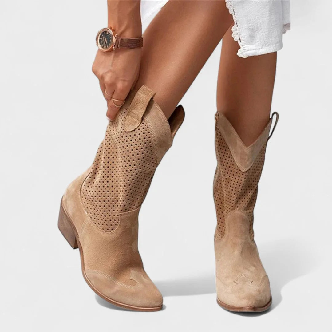 Woman adjusting a tan suede cowboy-style boot, showing pointed toe and perforated side panel texture