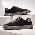 Pair of black suede trainers with grey soles and tan laces stacked on concrete blocks