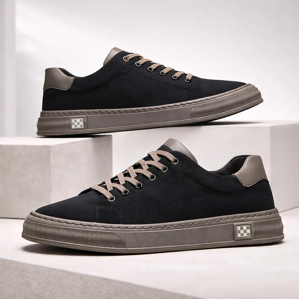 Pair of black suede trainers with grey soles and tan laces stacked on concrete blocks