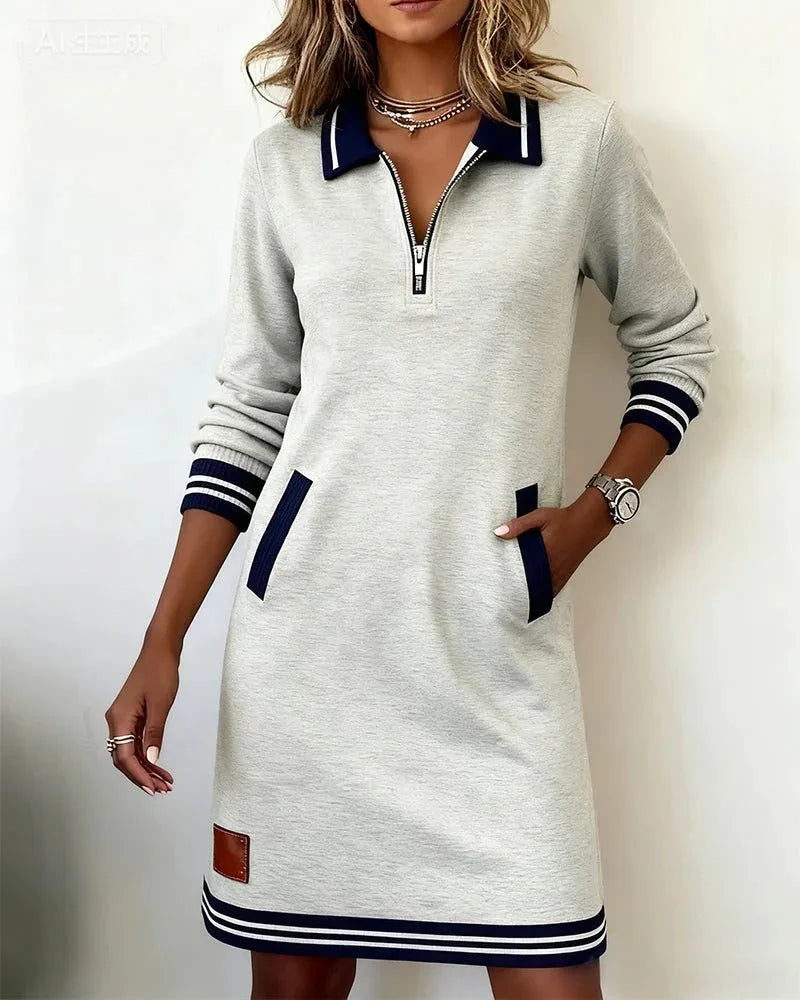 Front view of grey marl zip-collar sweatshirt dress with navy striped cuffs and welt pockets, styled with layered necklaces