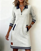 Front view of grey marl zip-collar sweatshirt dress with navy striped cuffs and welt pockets, styled with layered necklaces