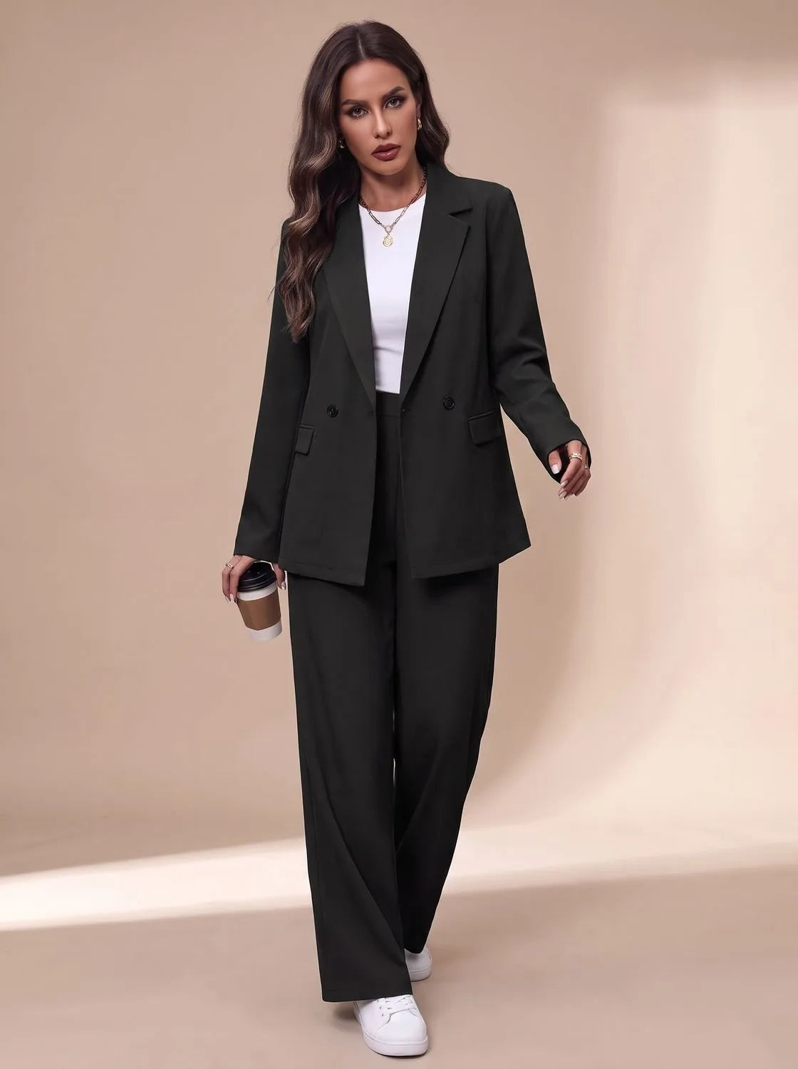 Front view of the dark green tailored two-piece suit with white top, white trainers and a coffee cup in hand