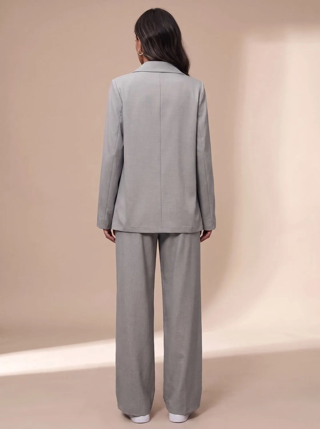 Close side view of the light grey blazer and trousers set, holding a coffee cup, showing fabric texture