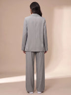 Close side view of the light grey blazer and trousers set, holding a coffee cup, showing fabric texture