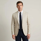 Beige linen-look blazer worn over a white shirt with a knitted navy tie and navy trousers