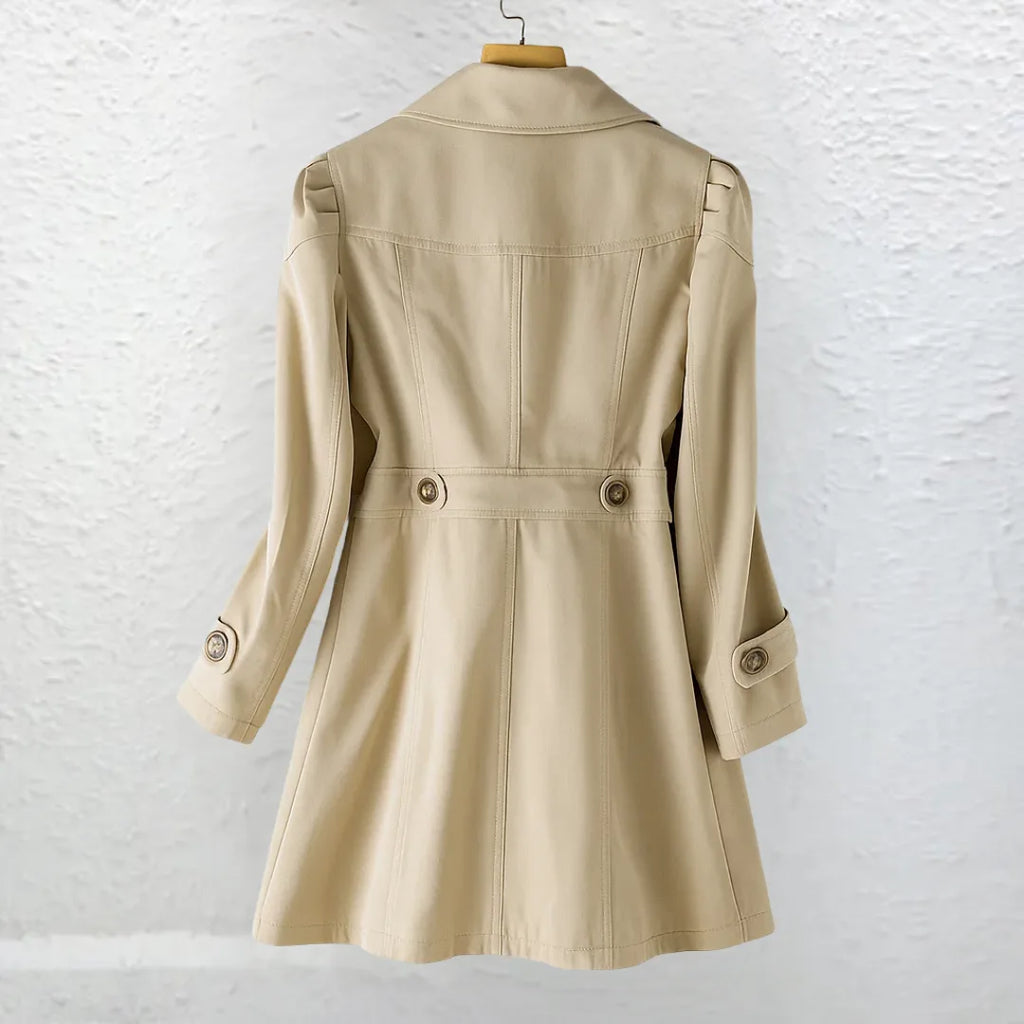 Back view of a beige trench-style coat on a wooden hanger, showing puffed shoulder seams and a fitted waist with button tabs