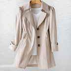 Close-up front view of a beige trench coat on a hanger, highlighting the wide collar, puff-shoulder seams and button cuffs