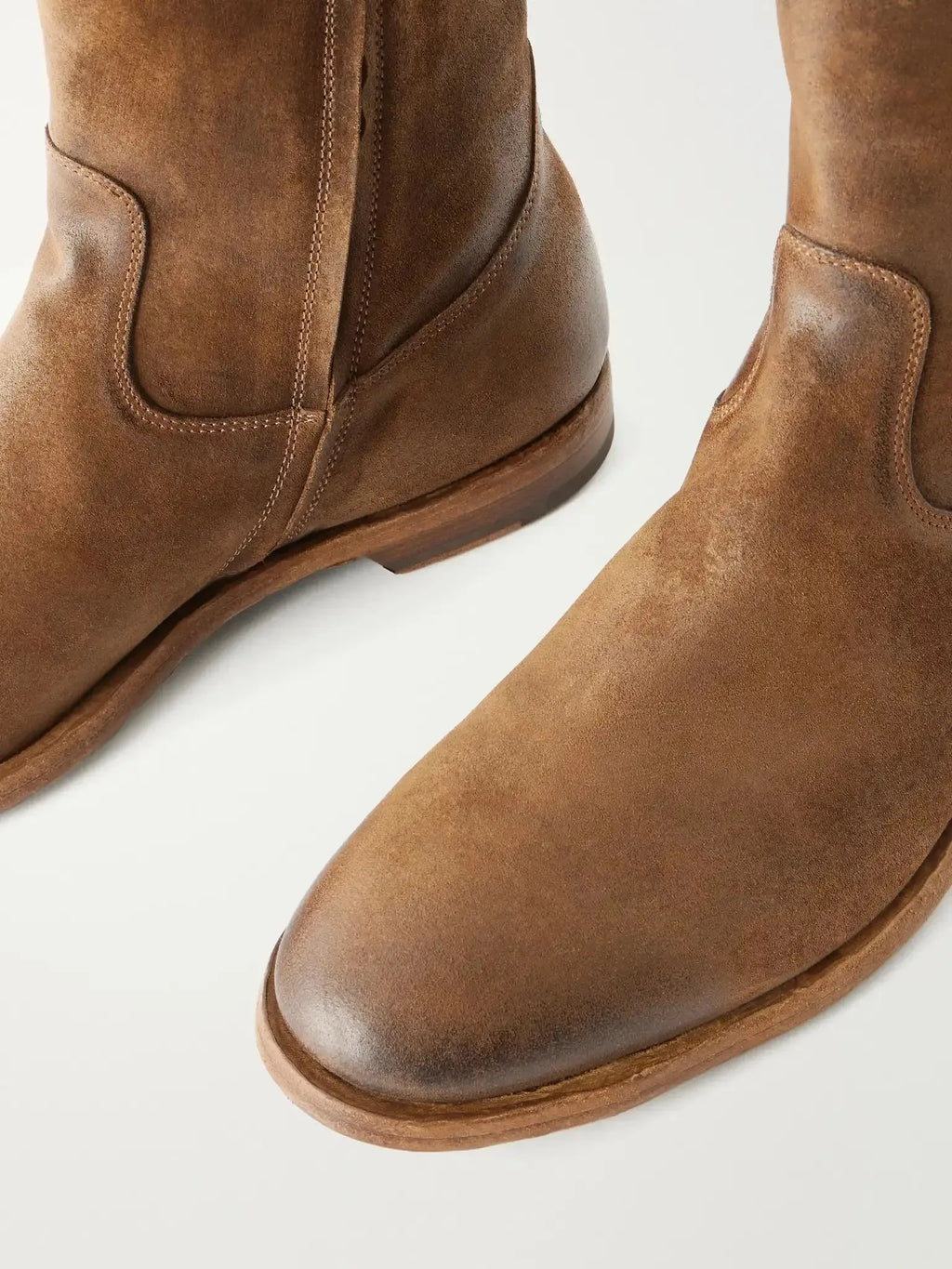 Close-up of two tan suede boots showing the rounded toe shape and weathered, distressed finish