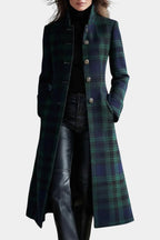 Front view of a woman wearing a green and navy tartan longline coat with stand collar over a black polo neck