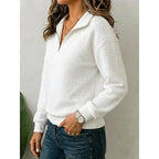 Side angle of a white textured quarter-zip jumper showing the ribbed cuffs and hem detail