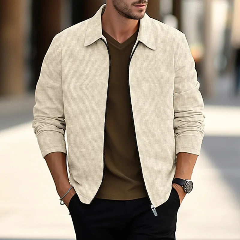 Man wearing a khaki textured overshirt, unzipped, layered over a brown polo neck with black trousers