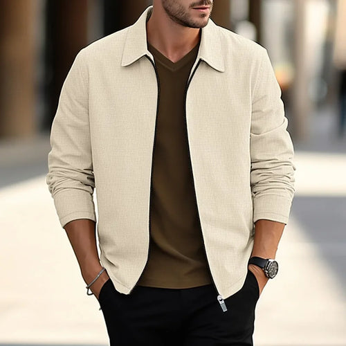 Man wearing a khaki textured overshirt, unzipped, layered over a brown polo neck with black trousers