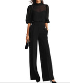 Woman wearing a black three-piece set with sheer mock-neck blouse, pleated wide-leg trousers and pointed heels