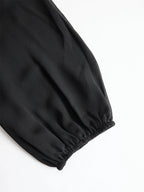 Close-up of the black blouse's puff sleeve showing the sheer chiffon fabric and elasticated cuff