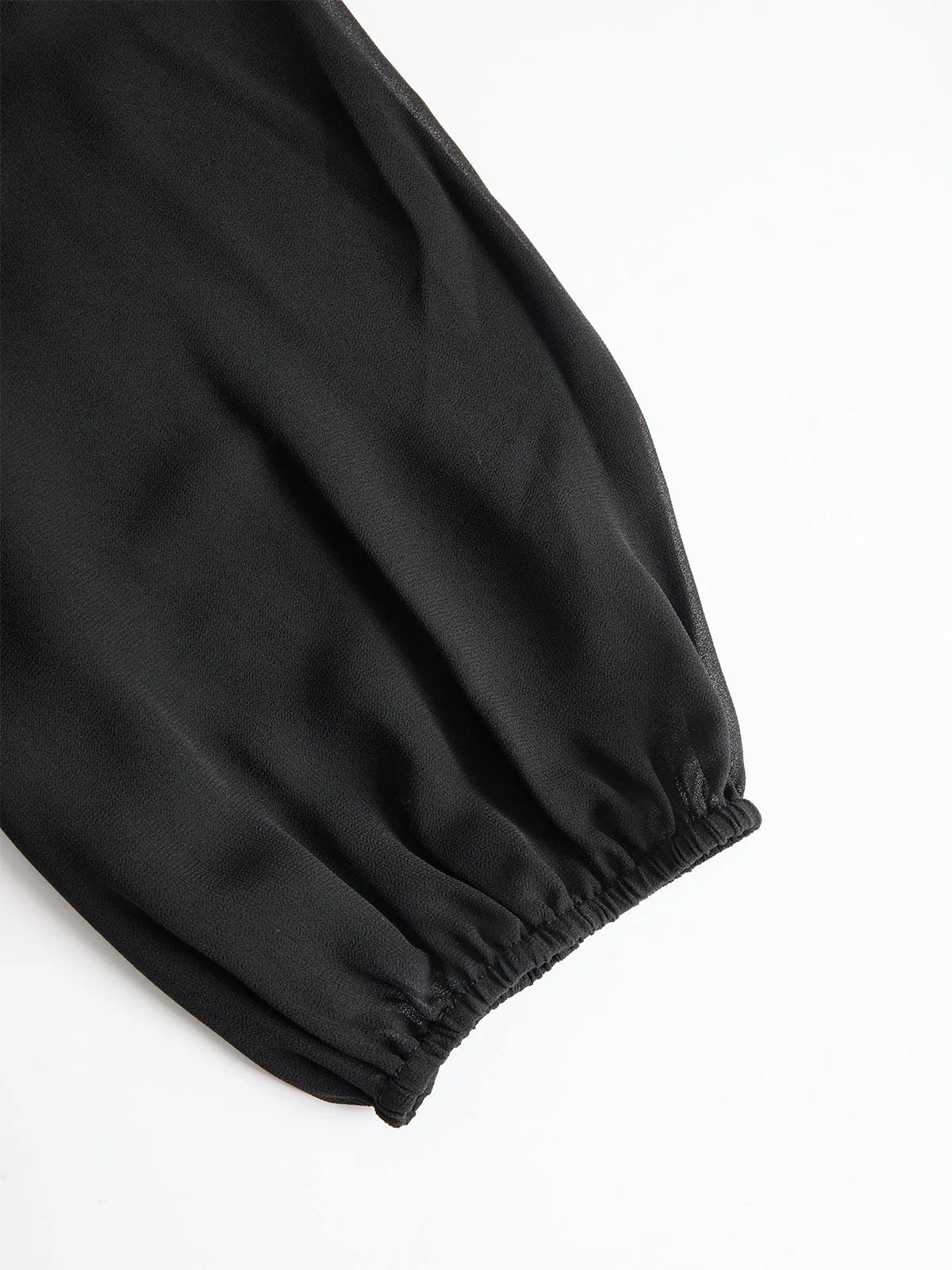 Close-up of the black blouse's puff sleeve showing the sheer chiffon fabric and elasticated cuff