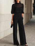 Full-length front view of the black three-piece set paired with a clutch bag and heeled shoes