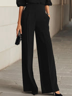 Close-up of the black wide-leg trousers showing the pleated front and smooth high waist