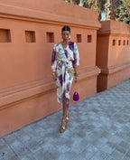Woman walking outdoors in a tie-dye wrap midi dress with front slit, gold platform sandals and a purple velvet bag