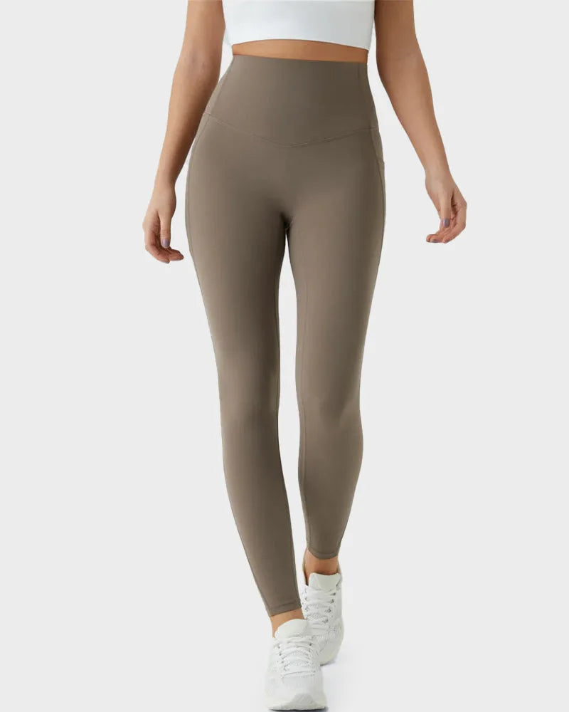 Front view of taupe leggings on model walking, showing sculpted waistband and slim ankle-length fit with white trainers