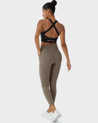 Full back view of model wearing taupe leggings with a black cross-back sports bra and hair in a bun