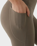 Close-up of a hand slipping into the deep side pocket of the taupe leggings, showing pocket depth and stitching