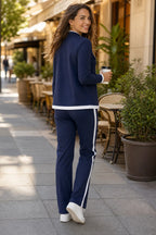 Back view on a city pavement showing the jacket's white hem trim and the trousers' side stripe down to white trainers