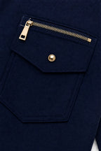 Close-up of a navy flap pocket with gold zip and matching gold snap button on the jacket