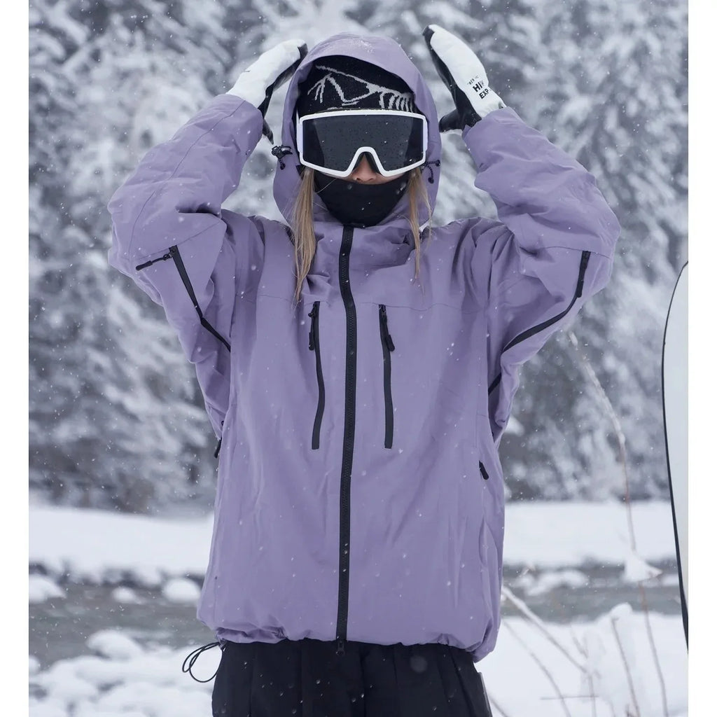 Close-up front view of a lilac purple ski jacket with hood pulled up and both hands raised to the hood