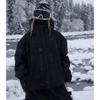 Model wearing an all-black ski jacket with hood up, standing by a snowy river bank