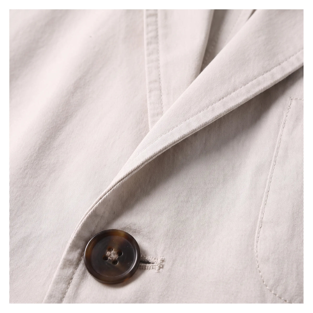 Close-up of the tortoiseshell-effect button and notch lapel stitching on the beige cotton blazer