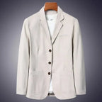 Beige cotton blazer on a wooden hanger against a dark background, front three-quarter view