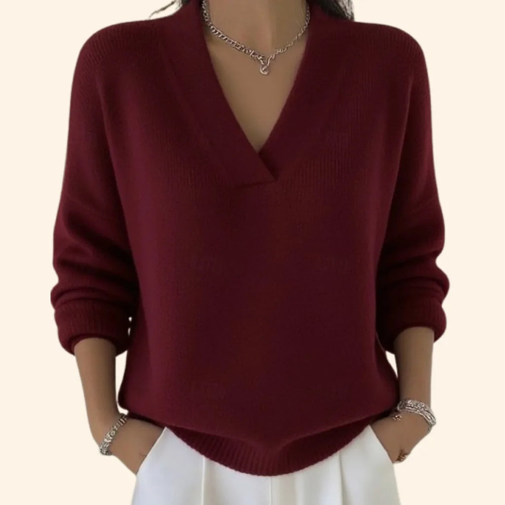Close-up of a woman wearing a burgundy V-neck jumper with dropped shoulders and ribbed cuffs, paired with white trousers