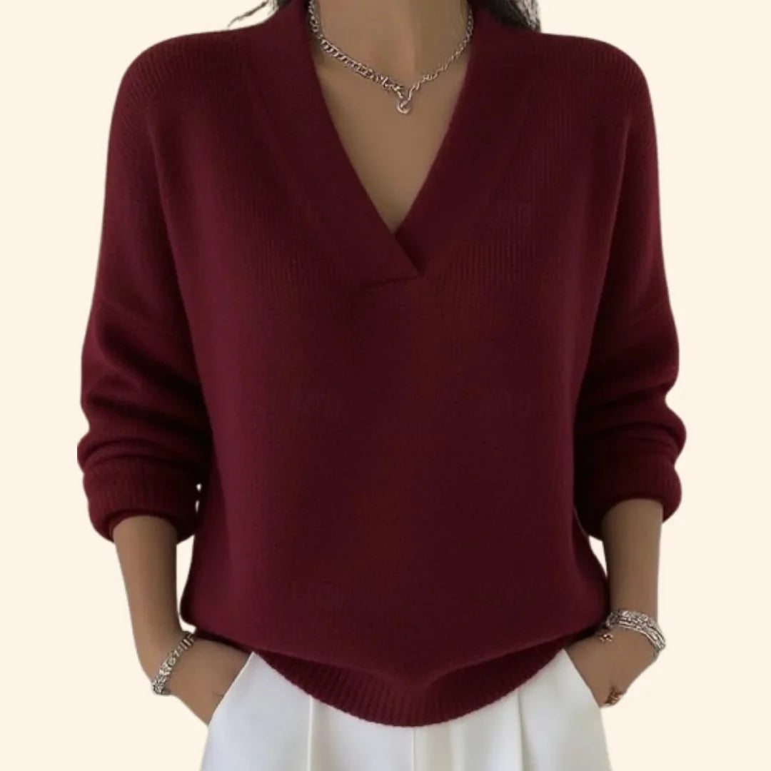 Close-up of a woman wearing a burgundy V-neck jumper with dropped shoulders and ribbed cuffs, paired with white trousers