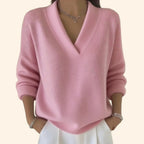 Front view of a soft pink relaxed-fit V-neck jumper with ribbed hem and long sleeves, styled with layered bracelets