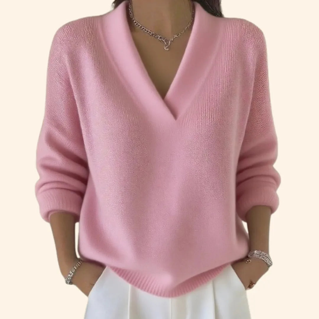 Front view of a soft pink relaxed-fit V-neck jumper with ribbed hem and long sleeves, styled with layered bracelets