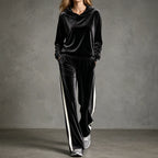 Woman walking in a black velour hooded tracksuit with cream side-stripe wide-leg trousers and zebra-print trainers