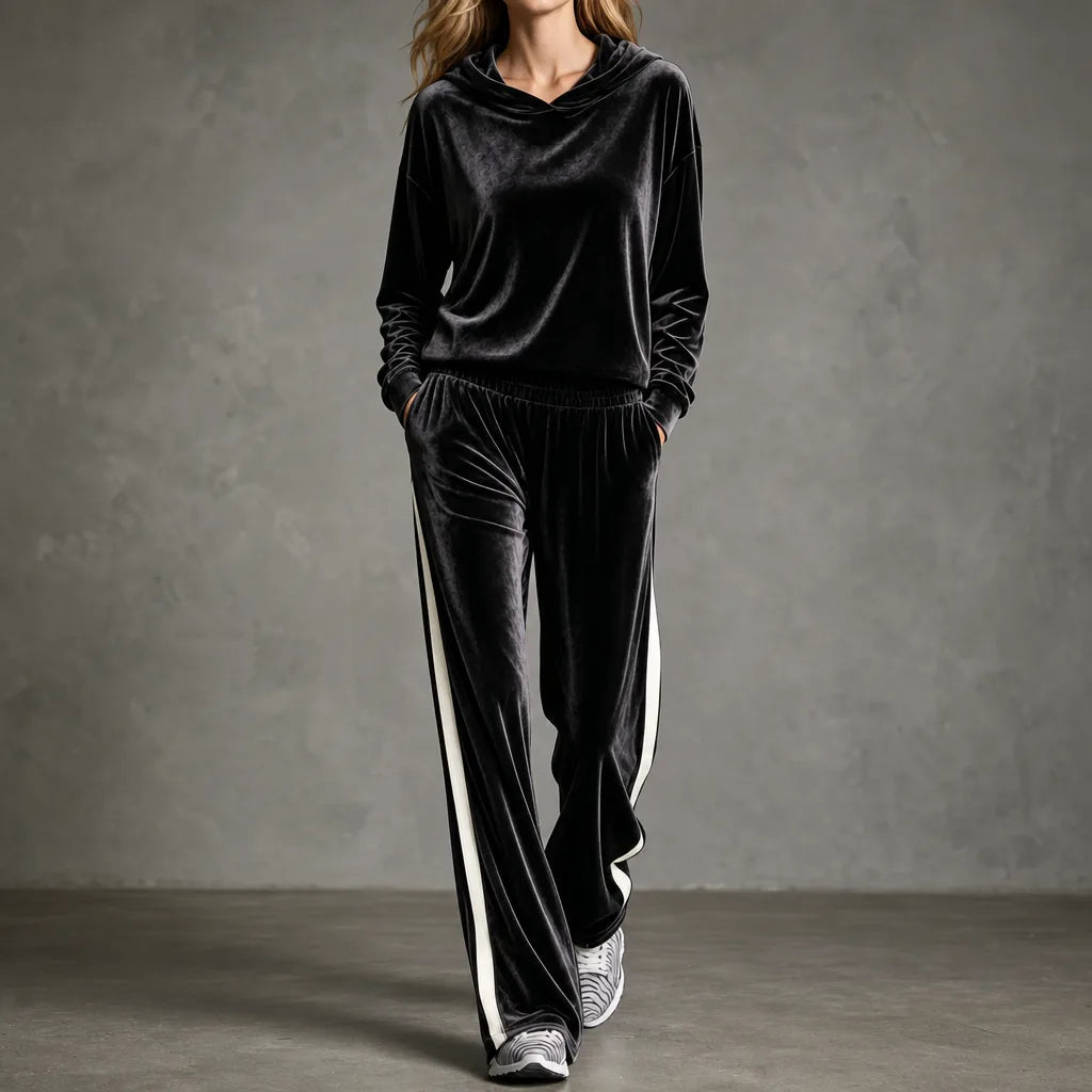 Woman walking in a black velour hooded tracksuit with cream side-stripe wide-leg trousers and zebra-print trainers