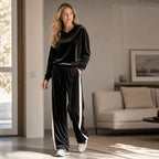 Full-length view of the black velvet tracksuit set styled in a bright living room with wide flowing trouser legs