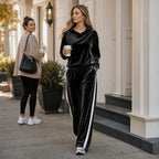 Woman wearing the black velour set with hood down, walking outdoors past storefronts holding a coffee cup