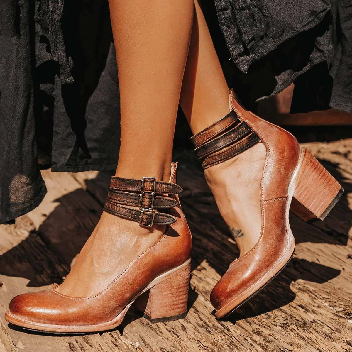 Dark brown distressed leather ankle strap heels with buckle straps and stacked heel, worn on feet