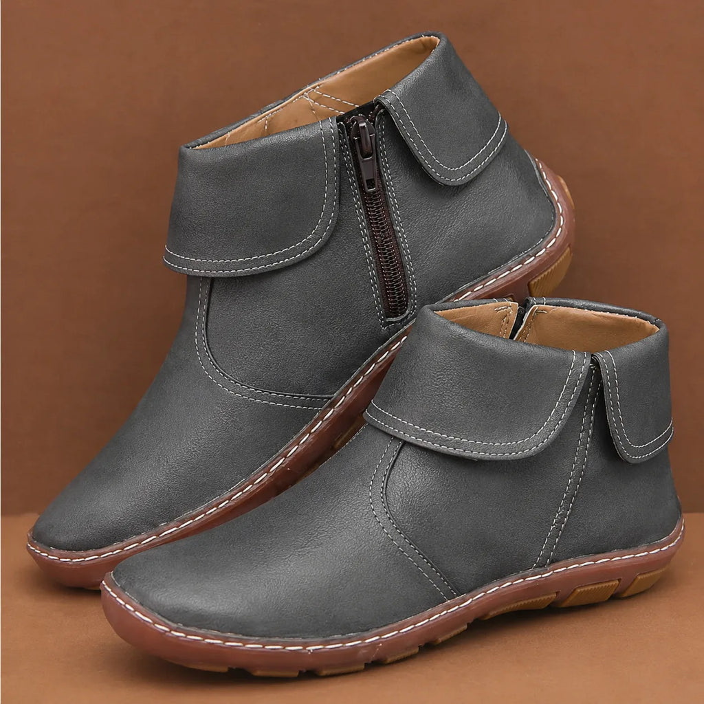Pair of grey leather ankle boots with foldover cuff, side zip and contrast stitching, shown against a brown backdrop