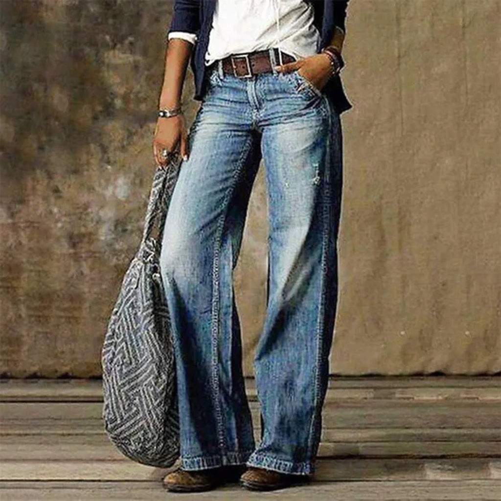 Front view of faded blue wide-leg denim jeans styled with a brown leather belt and navy blazer