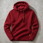 Red waffle-knit cowl-neck hoodie laid flat, showing ribbed hem and leather brand patch detail