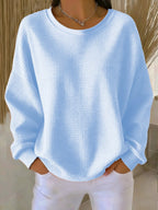 Model wearing a pale blue waffle-knit jumper with dropped shoulders and ribbed round neckline, hands in pockets
