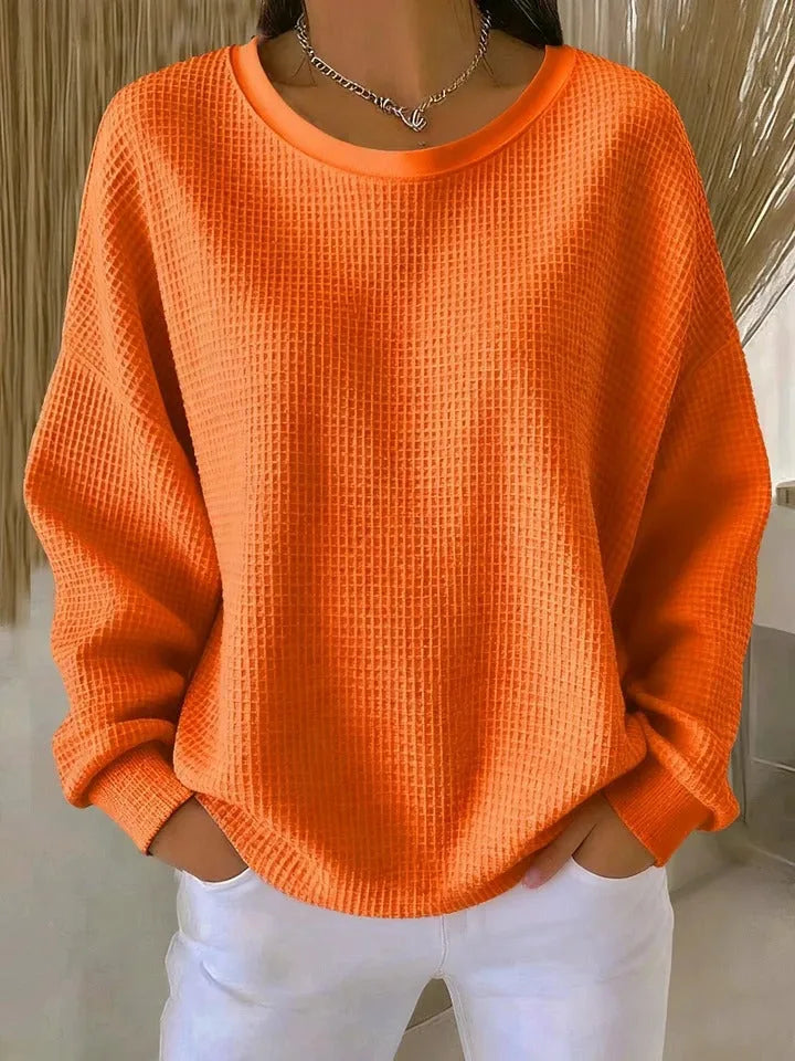 Bright orange waffle-knit jumper showing textured fabric detail and ribbed round neckline