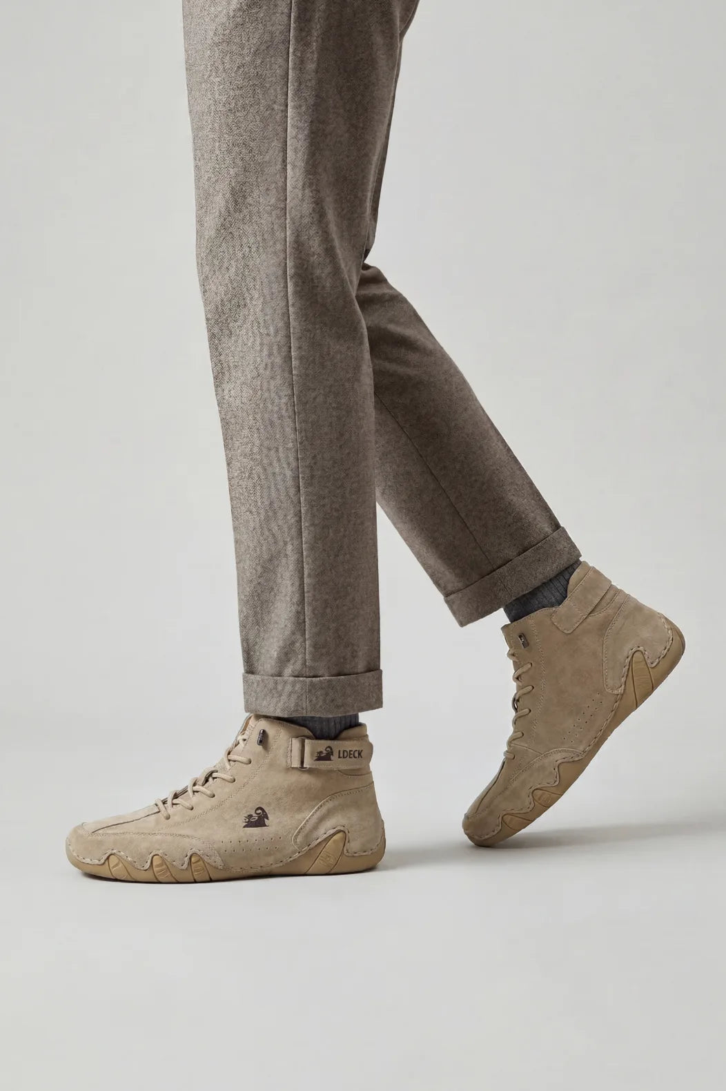 Man walking in beige suede high-top trainer boots paired with grey herringbone tailored trousers