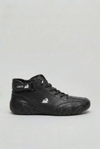 Side profile of the high-top boot in smooth black leather with a silver ram logo on the ankle strap